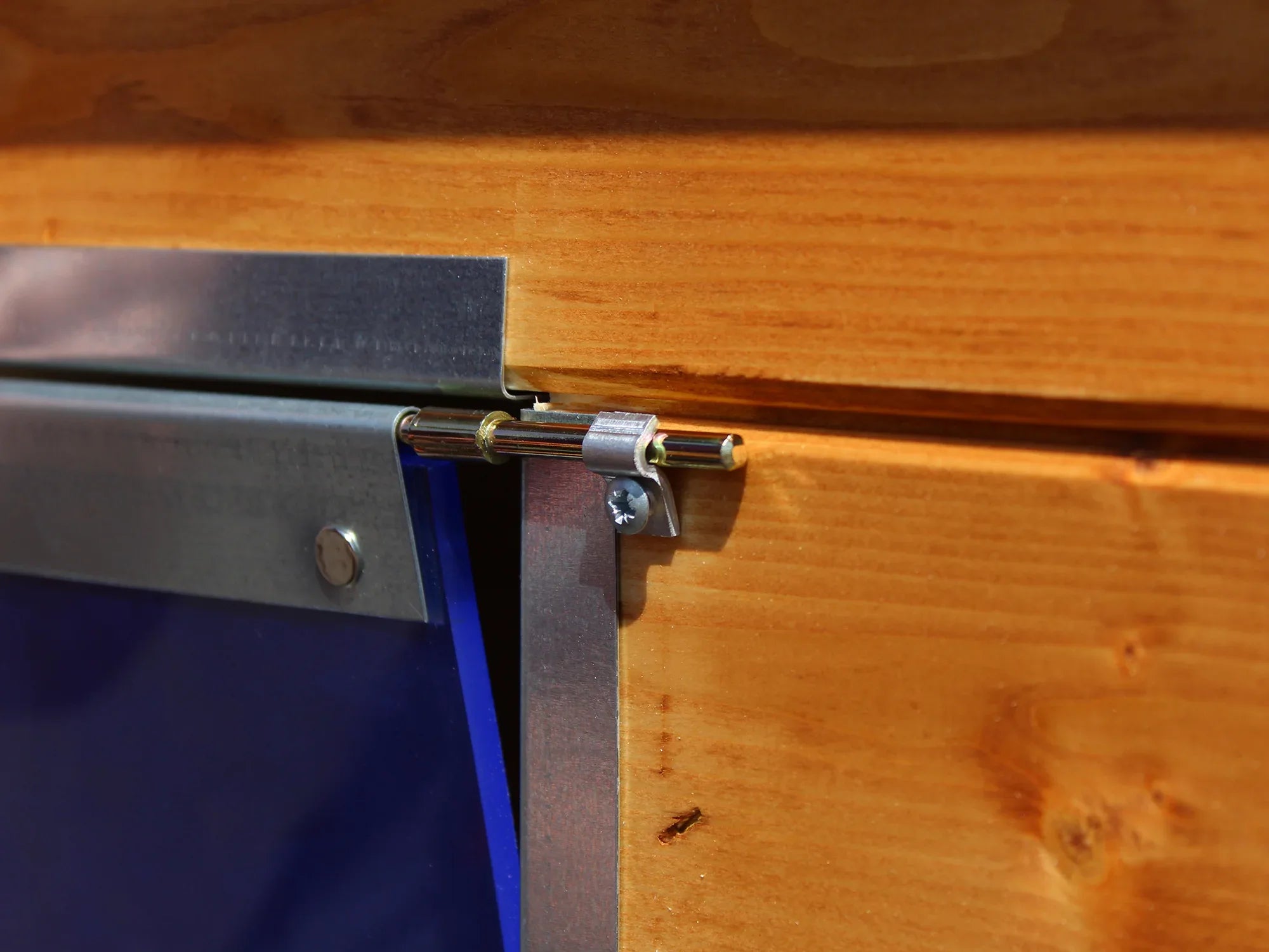 Befestigung einer blauen Pendelklappe mit Klammer und Schraube an einer Hundehüttenwand