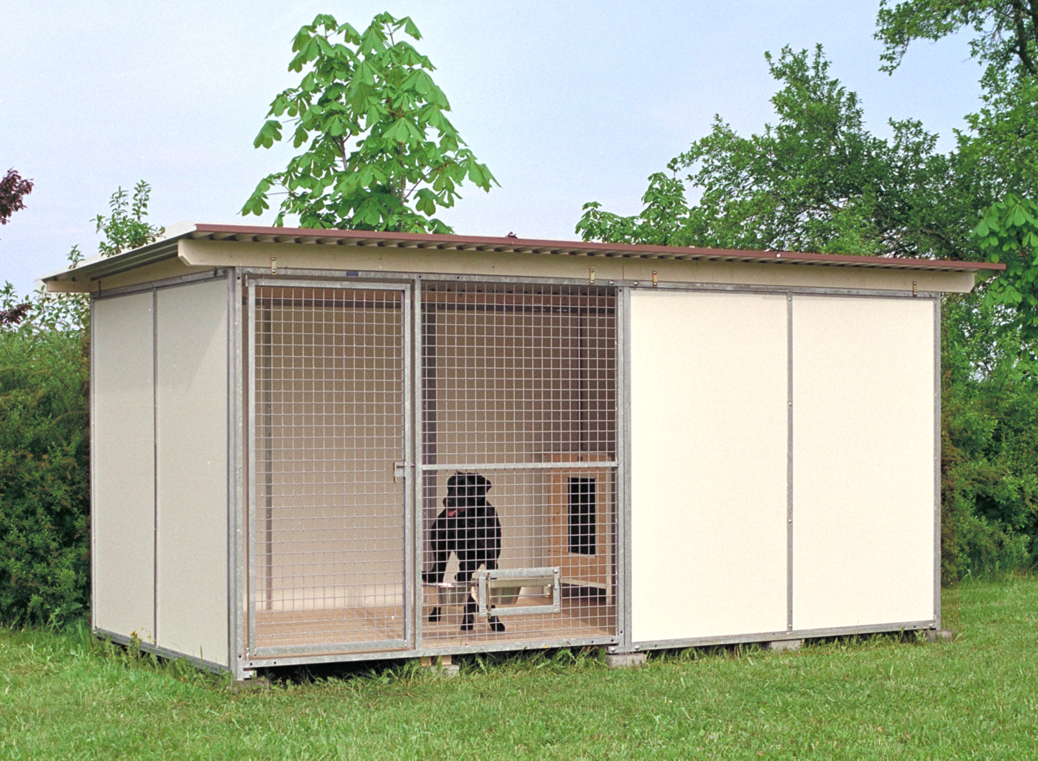 Hundezwinger mit Hundehütte und schwarzem Hund aufgebaut im Garten